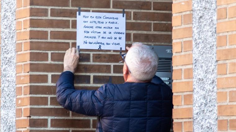 Un vecino del edificio donde se produjo el asesinato machista cuelga un cartel en el que se lamenta lo sucedido