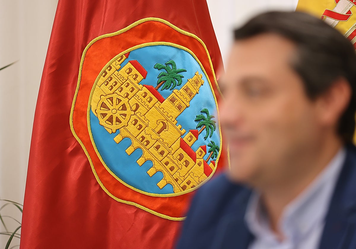 El alcalde de Córdoba, difuminado en primer plano, ante un escudo de la ciudad