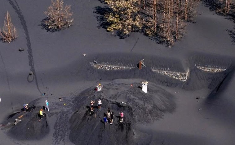 Imagen principal - Al quedar sepultada por la ceniza, Vicente puso una baliza para encontrar el lugar donde quedaba su casa y desentarrarla, ahora, con el auxilio de voluntarios