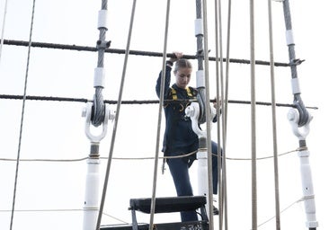 Con chándal azul marino y un arnés de seguridad, la Princesa Leonor sube a un palo de Elcano