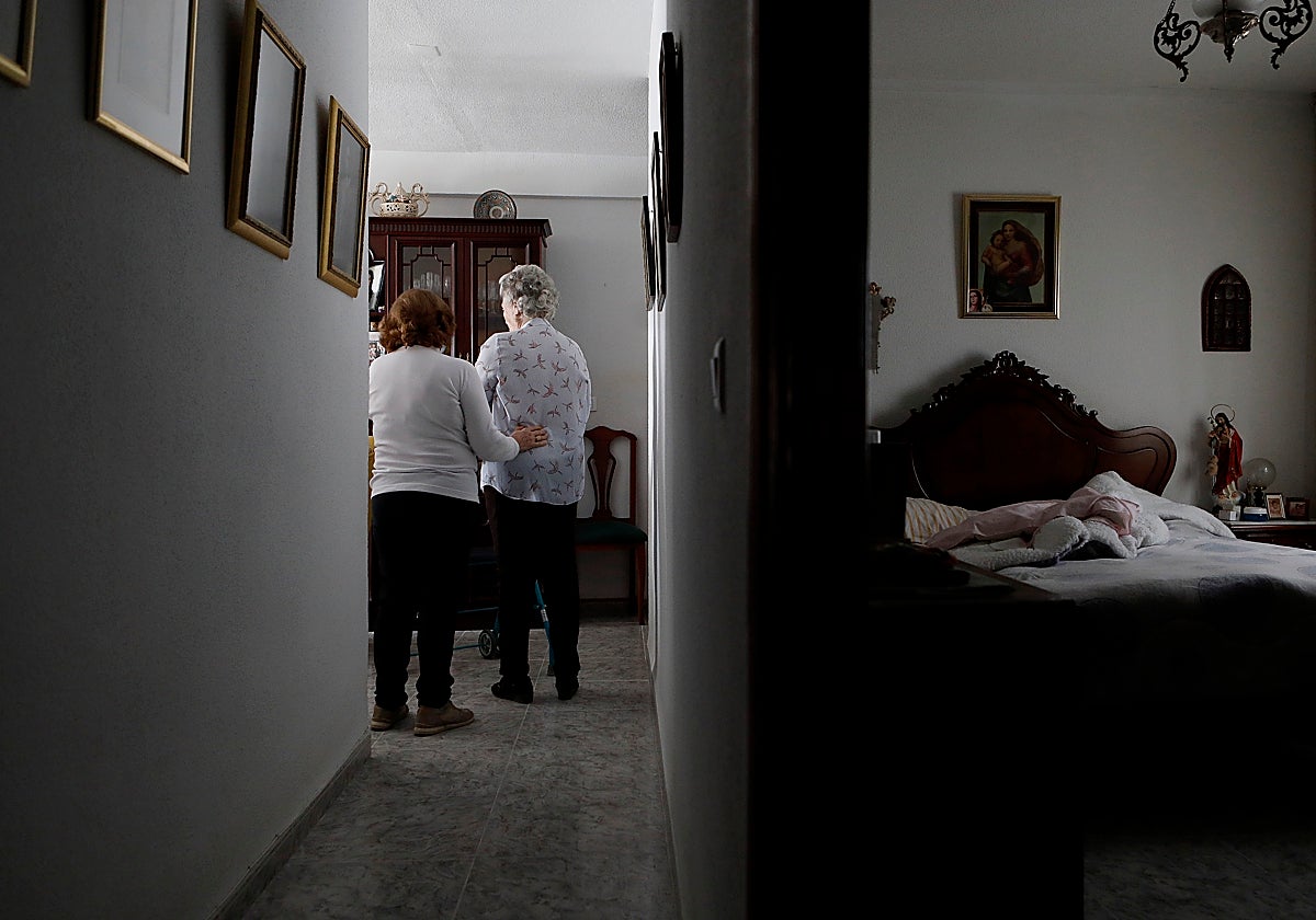 Una cuidadora sujeta a una mujer dependiente en su vivienda