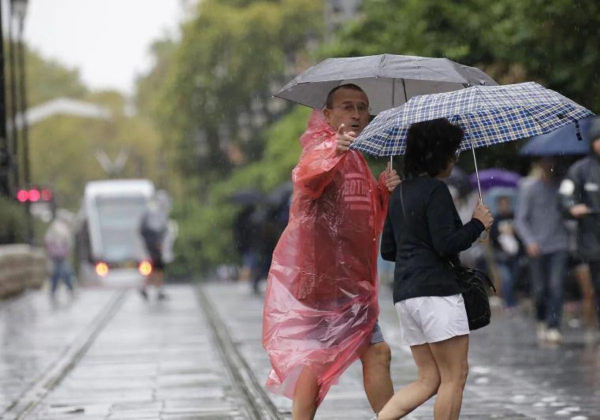 Dos personas con paraguas transitan por la Avenida de la Constitución de Sevilla