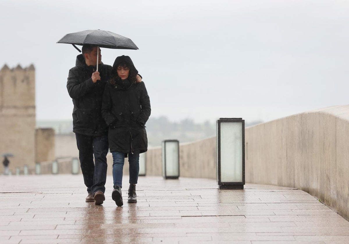 Dos personas cruzan el Puente Romano refugiándose de la lluvia
