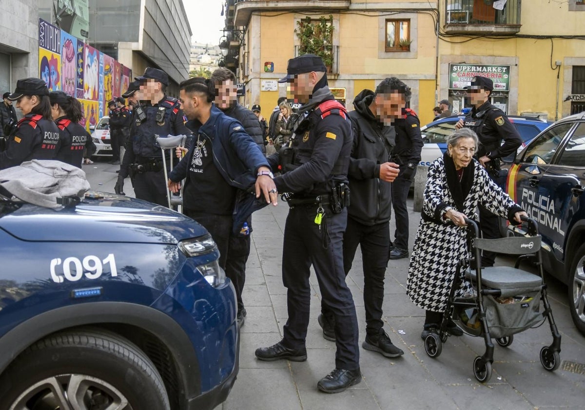 Agentes de los Mossos y la Policía Nacional durante el registro a varios multirreincidentes en el Raval. Uno de los funcionarios, ayuda a una anciana a avanzar en medio del despliegue