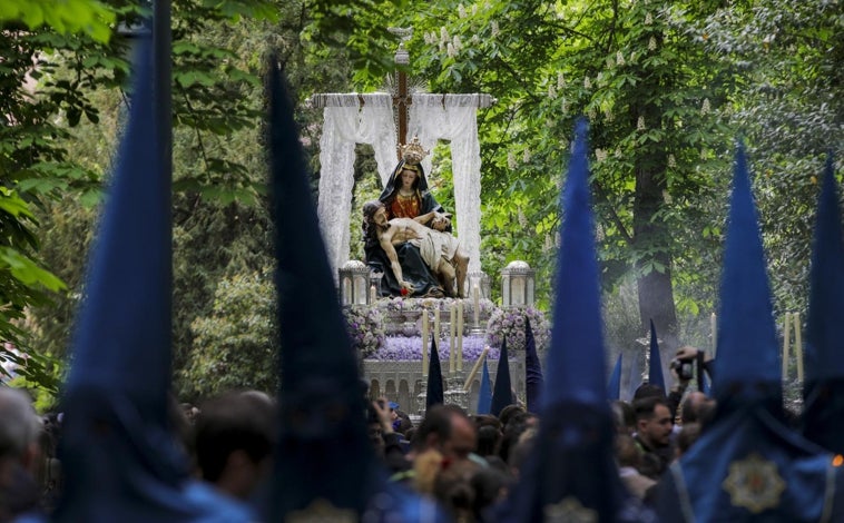 Imagen principal - La Virgen va por los jardines cargada por costaleros y un amplio cortejo de nazarenos. 