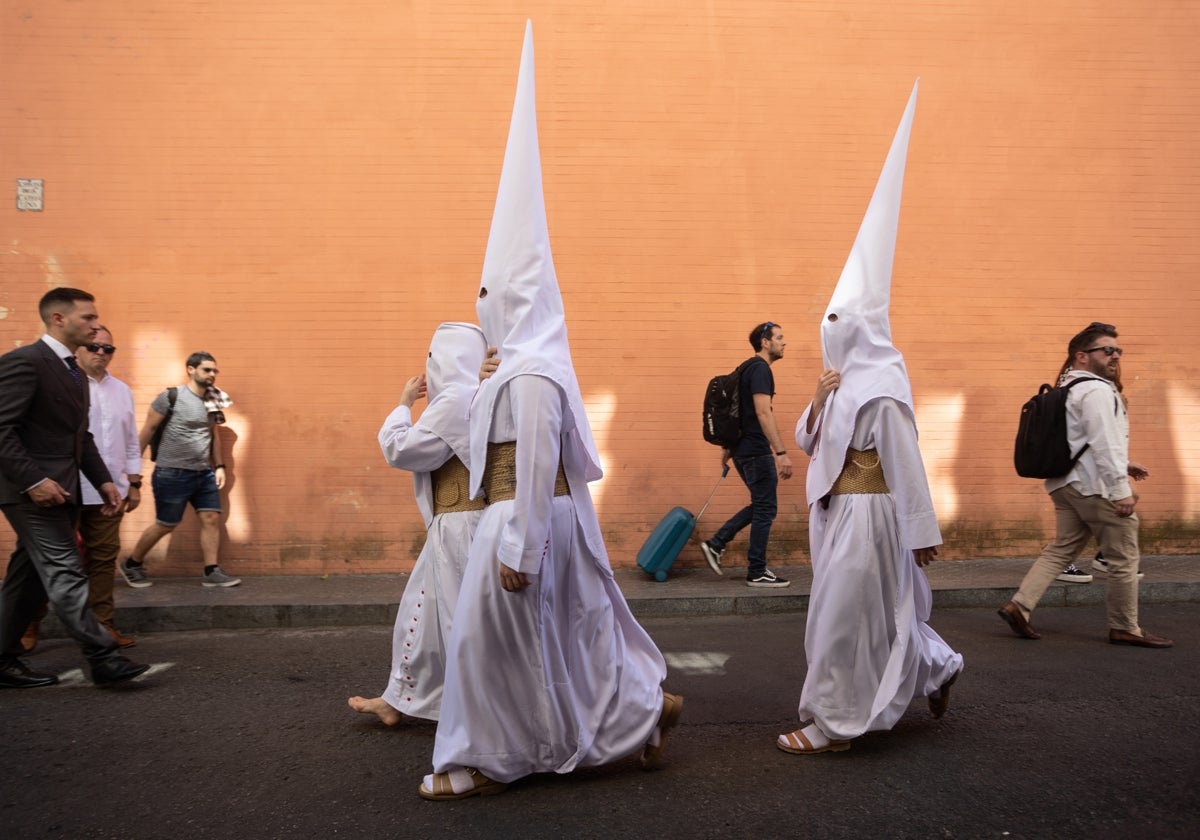 Varios turistas pasan junto a nazarenos de la hermandad de la Cena en Sevilla