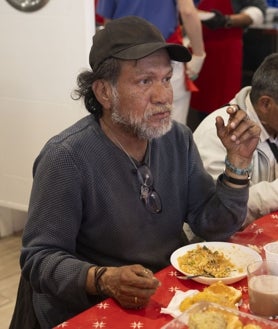 Imagen secundaria 2 - Los asistentes esperan en fila para recibir el número de su turno para comer; Tino, quien organiza el acceso al Comedor Social San Juan Bautista, con la pequeña Anyelis y sus dos hermanos; y otro de los usuarios, ya sentado a la mesa