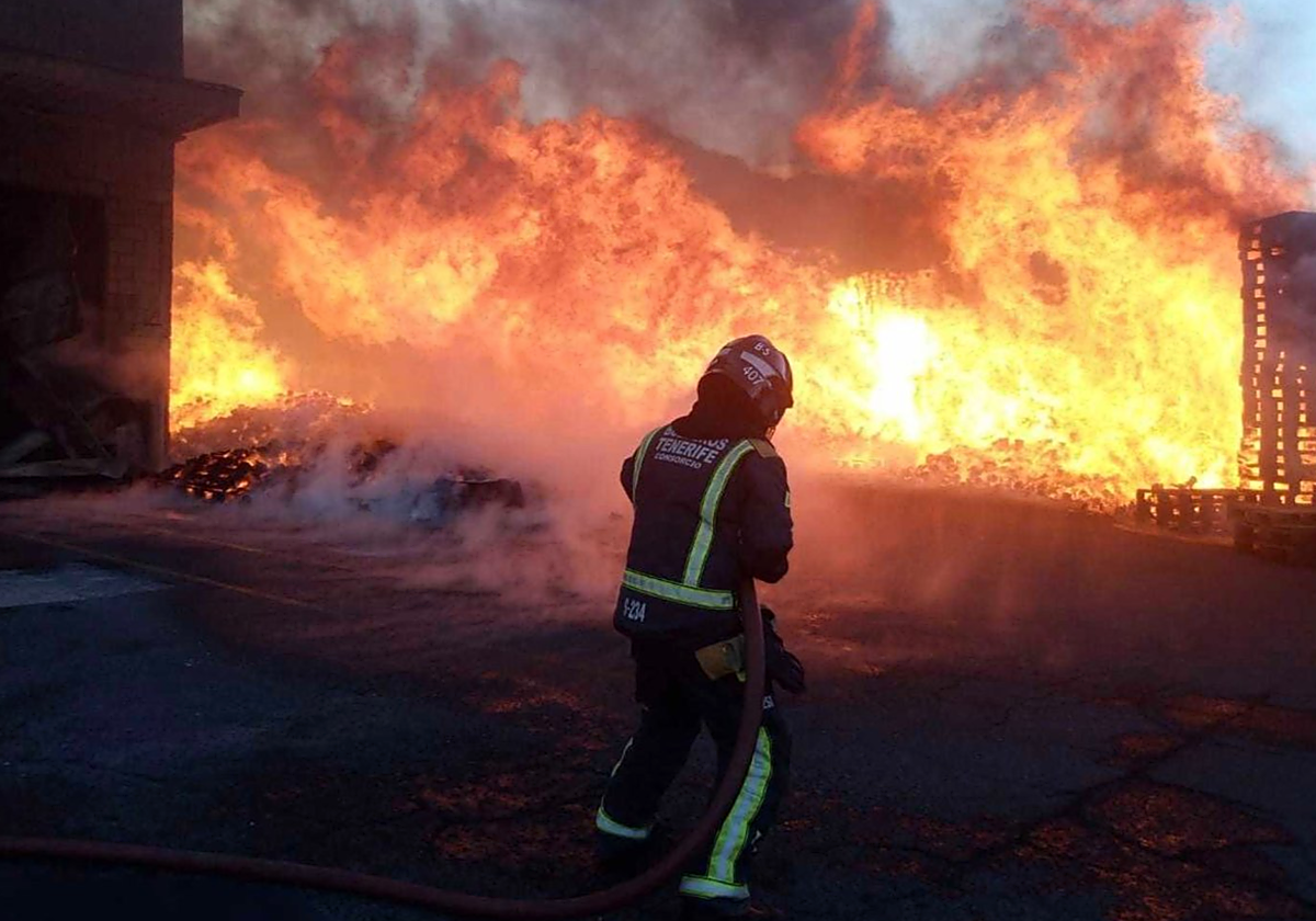 Un agente de los bomberos de Tenerife lucha contra las llamas de la nave industrial