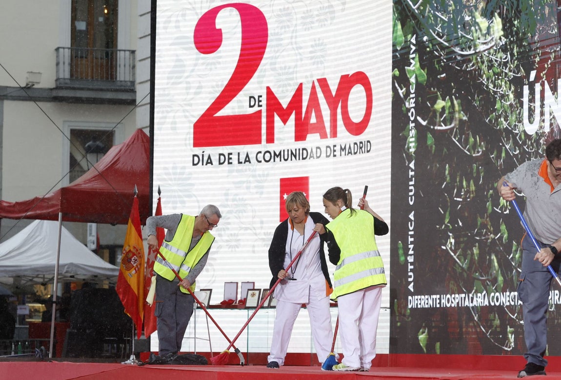 Varios operarios achican agua del estrado para el homenaje a los Héroes del Dos de Mayo en Madrid.