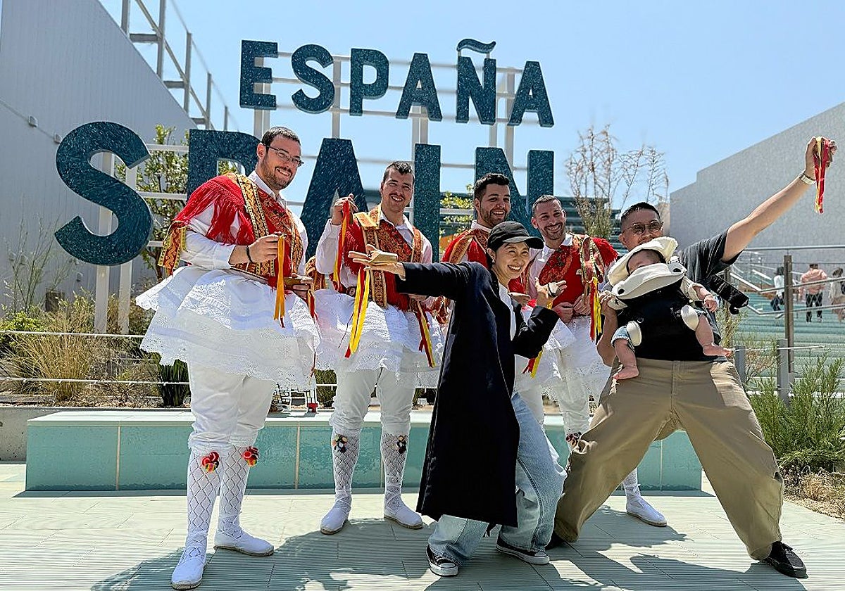 Dos visitantes japoneses se hacen una fotografía con danzantes del paloteo