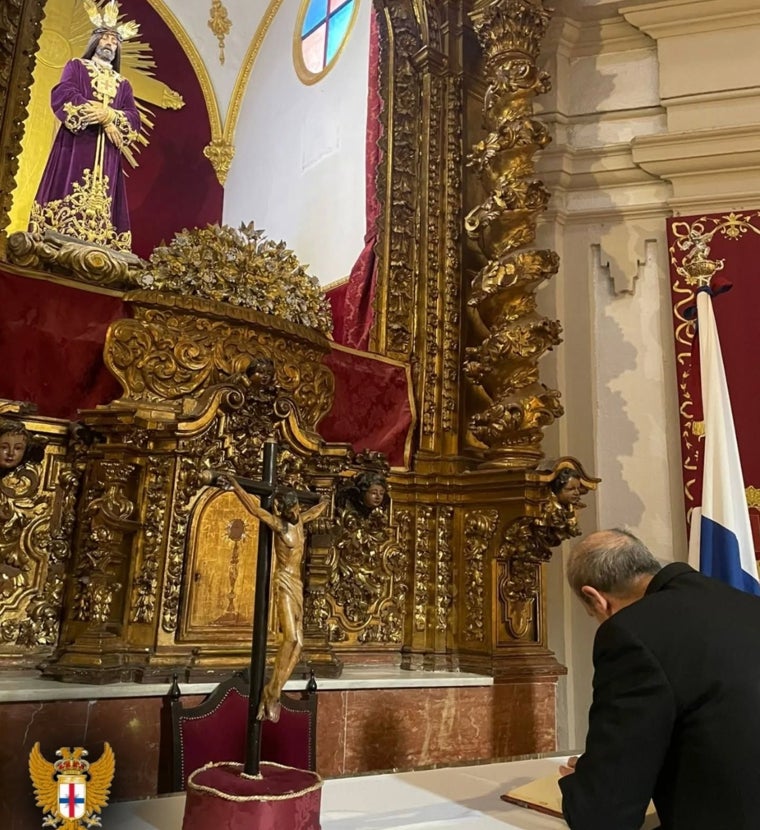 El obispo, Jesús Fernández, firma en el libro de visitas de la hermandad, ante el Rescatado