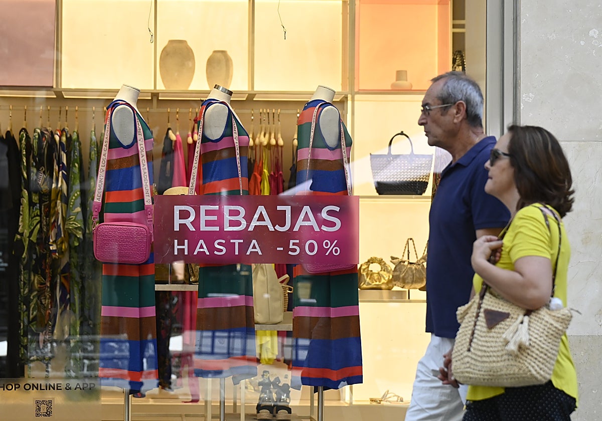 Una pareja de cordobeses pasea frente a un escaparate en rebajas del centro de la capital