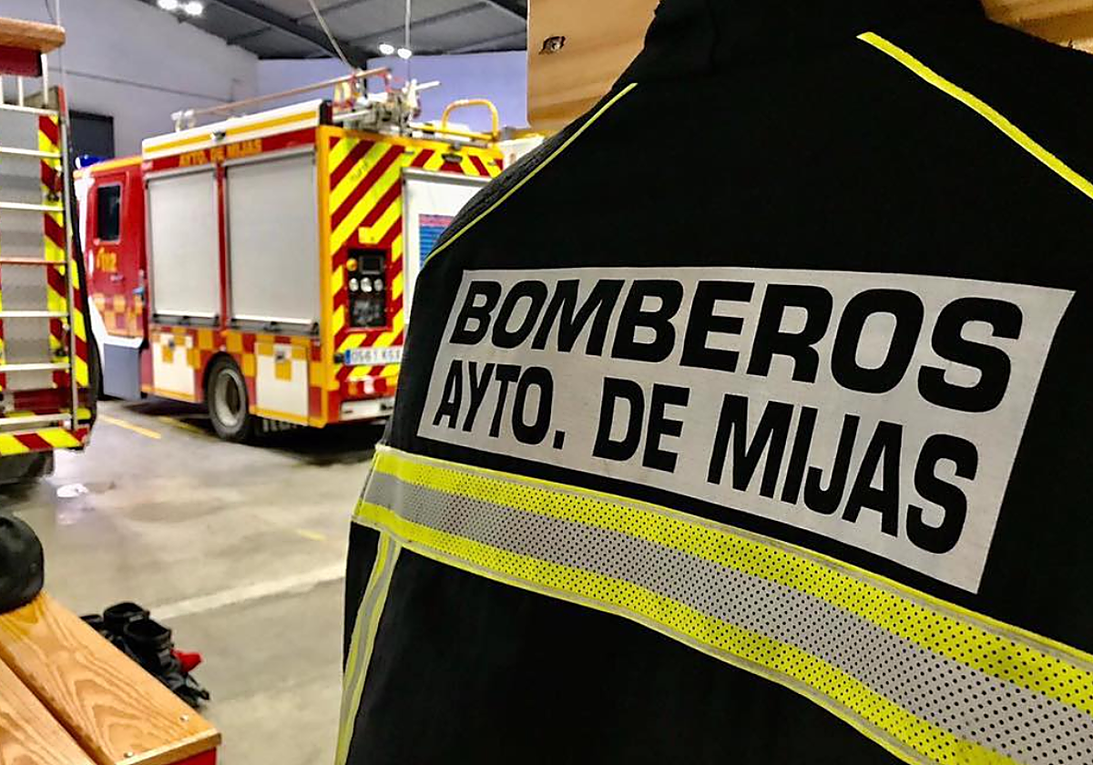 Foto de un chaleco de bomberos de la zona de Mijas junto a varios camiones para apagar incendios