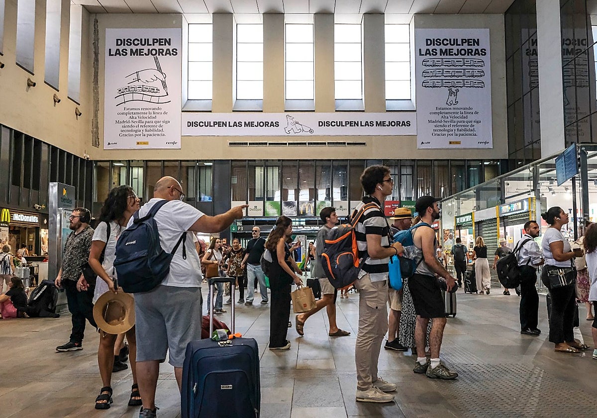 Viajeros, esperando en la estación de Santa Justa, con el polémico cartel al fondo.
