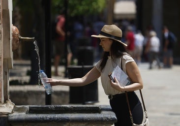 Una joven llena una botella de agua en una fuente en Córdoba