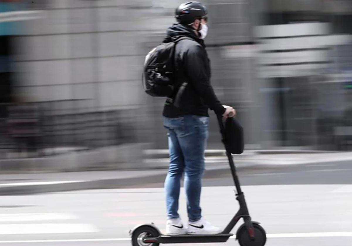 Un chico conduce un patinete eléctrico por la ciudad en foto de archivo