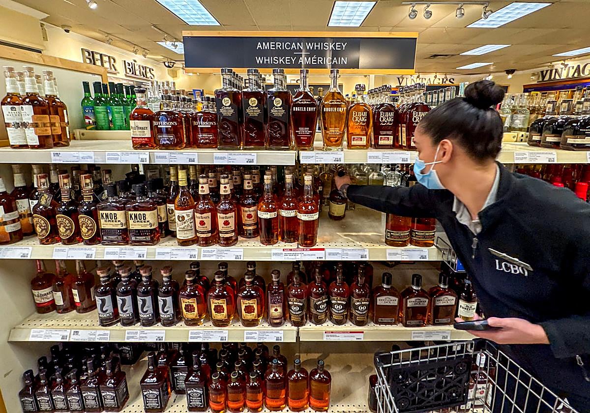 Una mujer coloca botellas de whsikey en un supermercado.