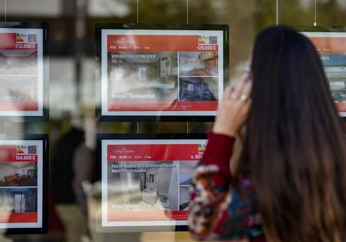 Una chica mira los carteles de oferta de pisos en venta y alquiler en una inmobiliaria en foto de archivo