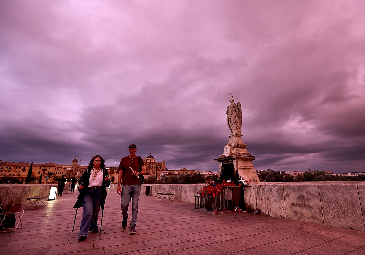 Dos personas pasean por el Puente Romano con nubarrones en el cielo