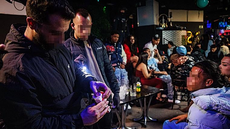 Two plainclothes agents search for drugs among the young men's possessions in the nightclub