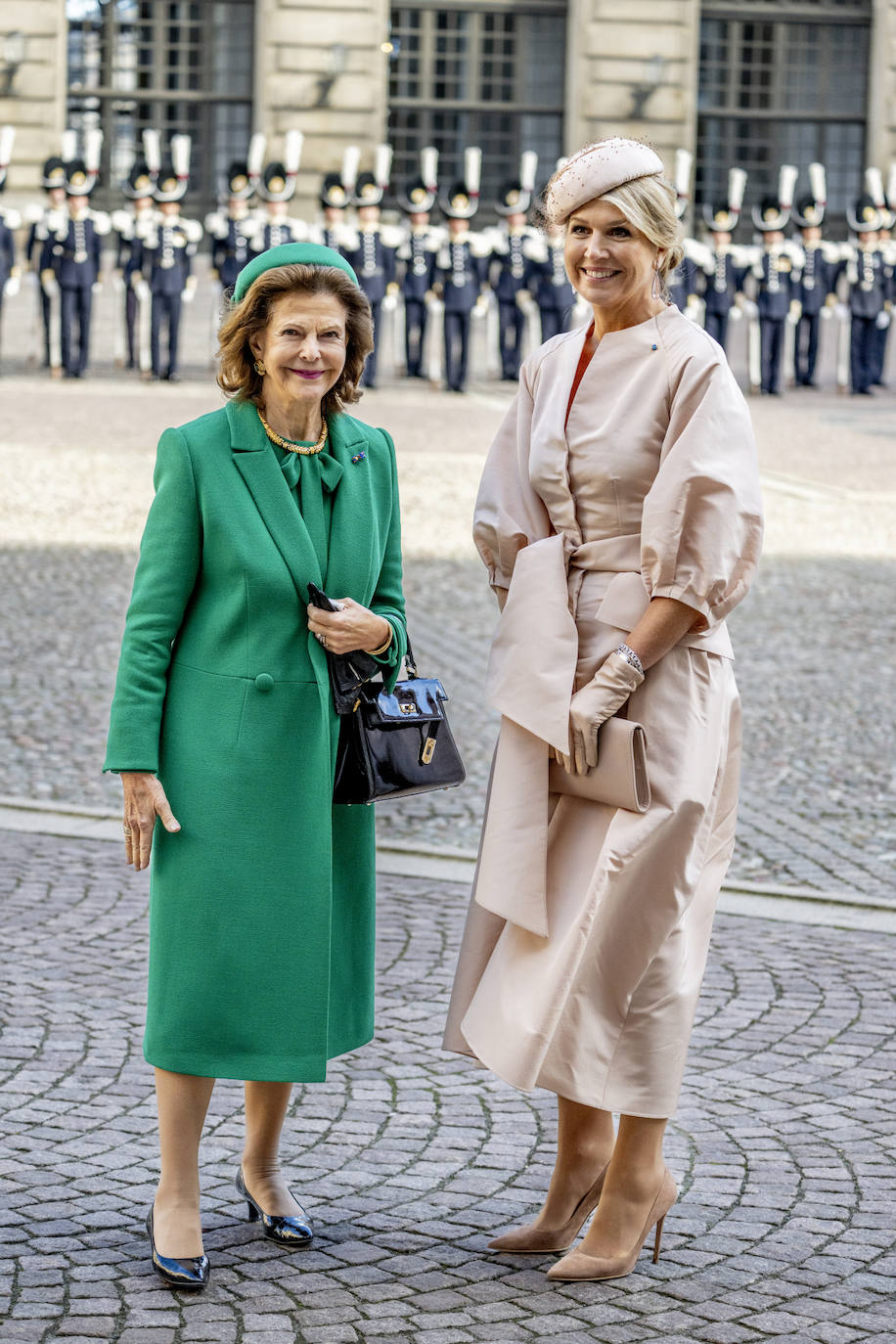 Posteriormente fueron recibidos por los reyes de Suecia. En esta imagen, junto a la reina Silvia, se aprecia mejor el estilismo de Maxima. Se trata de un vestido-abrigo de la firma belga Natan, una de las habituales de su armario. Lo combinaba con guantes y tocado en el mismo tono, así como stilettos de ante nude y cartera también nude. Además, llevaba pendientes en forma de lágrima, de oro blanco y diamantes.