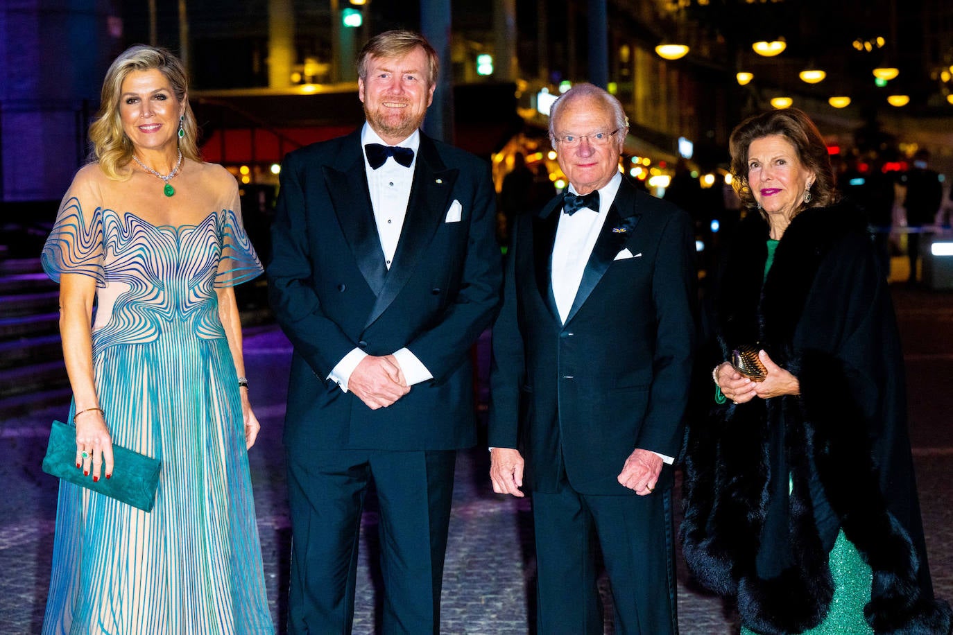 Por la noche, para acudir a un concierto del violinista Tim Kliphuis, Máxima de Holanda recuperaba el vestido que estrenó durante la celebración en Amsterdam de su 50º cumpleaños. Se trata de un diseño de Iris Van Herpen, semitransparente, con forro nude y decorado con ondas en azul petróleo. Como complementos eligió un espectacular conjunto de pendientes y colgante con esmeraldas. Además llevó una cartera de ante en color verde y sandalias de tacón fino.