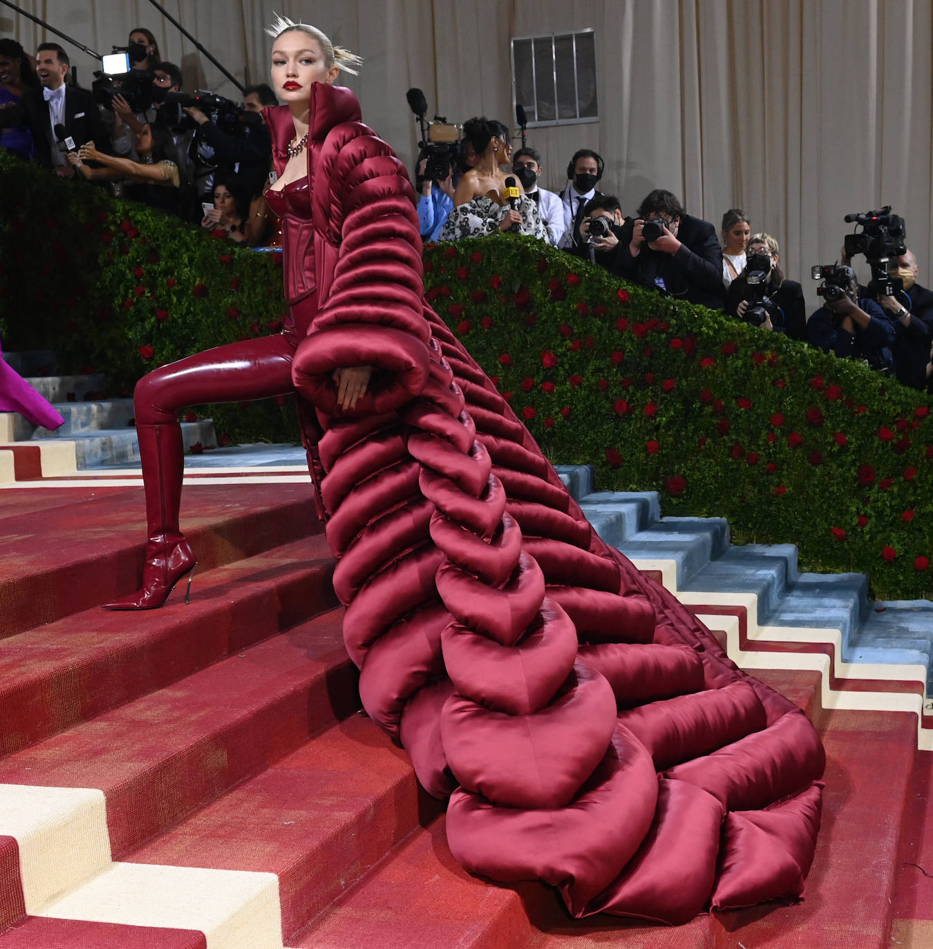 Gigi Hadid en la Gala Met 2022 con mono de látex burdeos con cuerpo encorsetado que conjuntó con un plumas XXL de Versace.