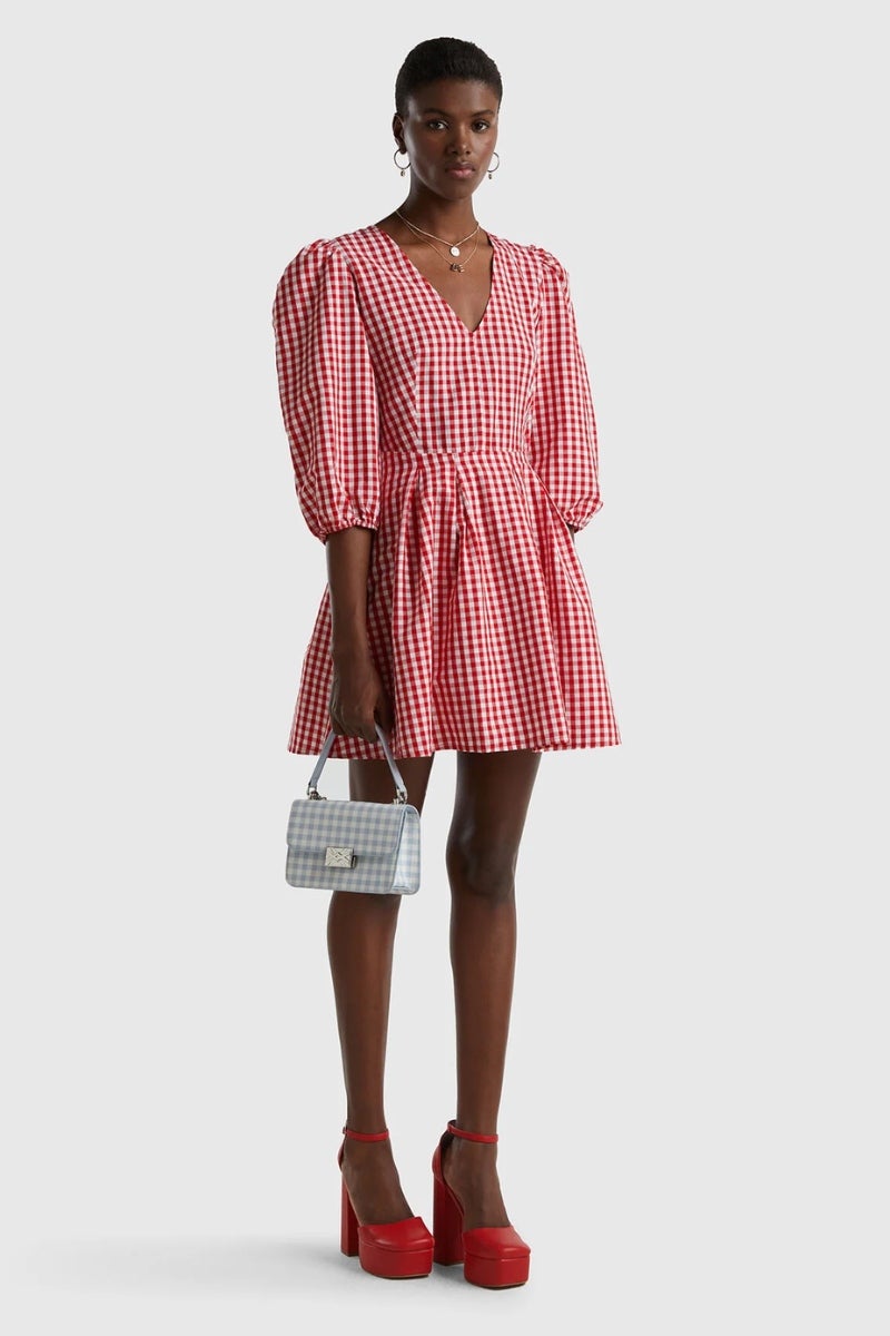 Vestido corto de Vichy, de Benetton. Un modelo que también está disponible en versión infantil para que madres e hijas puedan ir conjuntadas. La prenda posee escote en pico, manga abullonada, pliegues en la cintura y una falda cargada de vuelo. Precio: 89,95€.