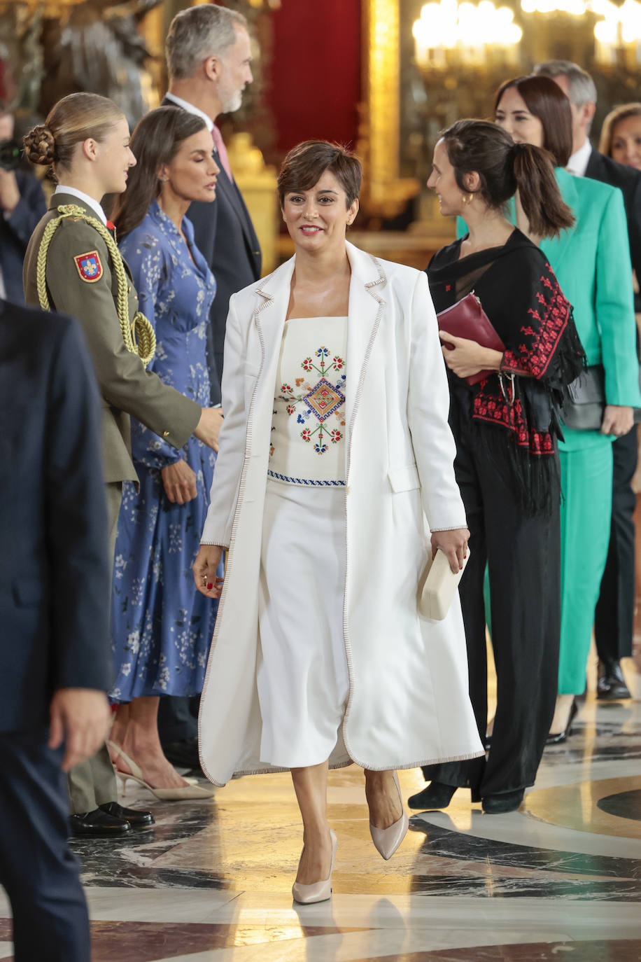 Isabel Rodríguez García, Ministra de Política Territorial y portavoz del Gobierno en funciones, de blanco, con falda y top con estampado étnico y trench en el mismo tono. Es un look de JCPajares, realizado en colaboración con dos artesanas de la firma. El look se compone de un corsé de lino reciclado bordado en Lagartera, un trabajo maestro de 70 horas que formó parte de la colección recién presentada en la Mercedes-Benz Fashion Week Madrid. Complementando esta pieza,  lució una americana de hombros XL y largo midi adornada con 'damas' bordadas y rematada”con botones de cerámica junto con una falda midi, ambas piezas confeccionadas en crepe.