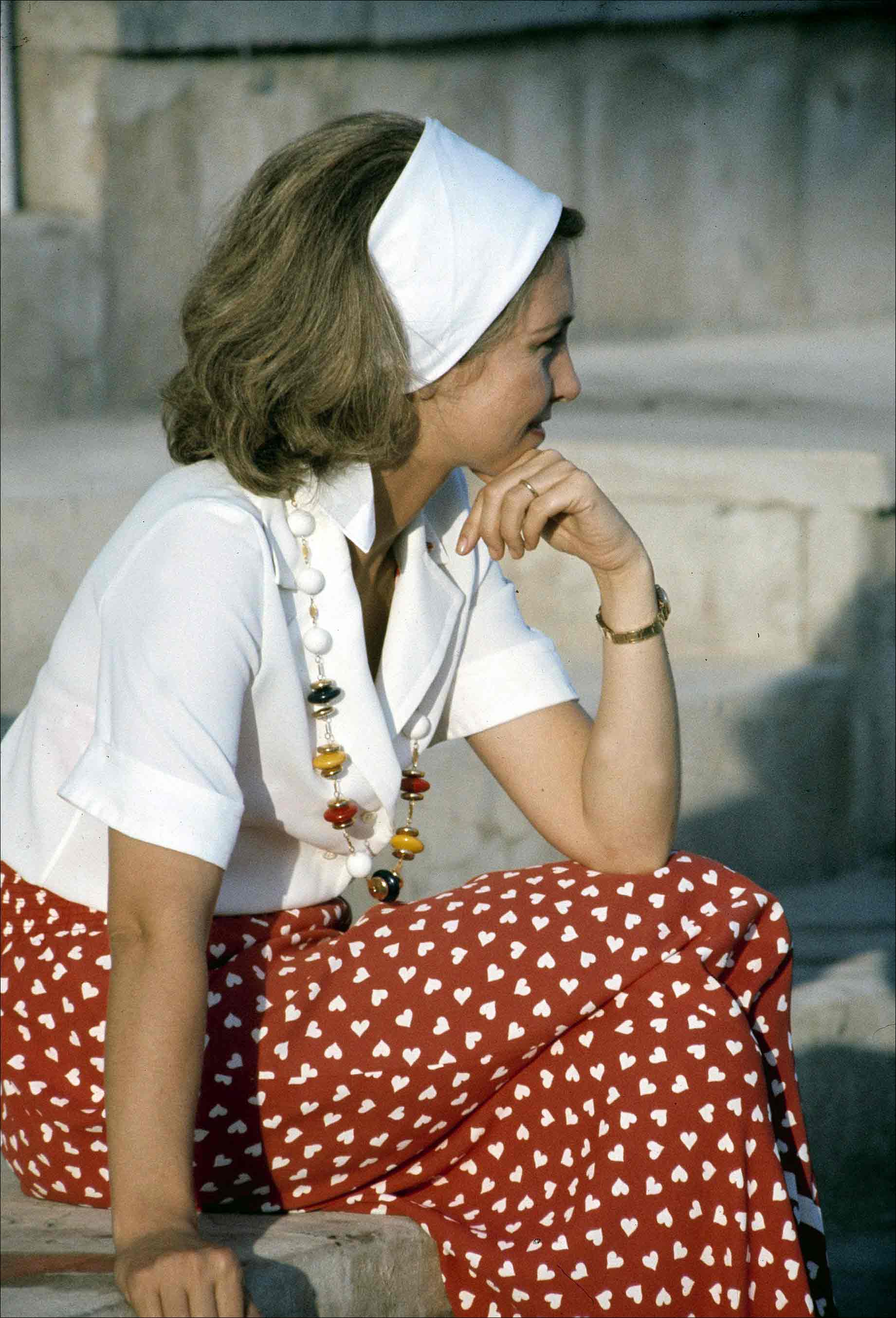 La Reina Sofía, con un pantalón en tonos rojos con estampado de corazones blancos y un top blanco de manga corta con escote cruzado de solapas. Como buena amante de la moda, eligió unos complementos de lo más especiales, con un collar de perlas y borlas de colores y una amplia diadema, un accesorio que vuelve a estar en tendencia.