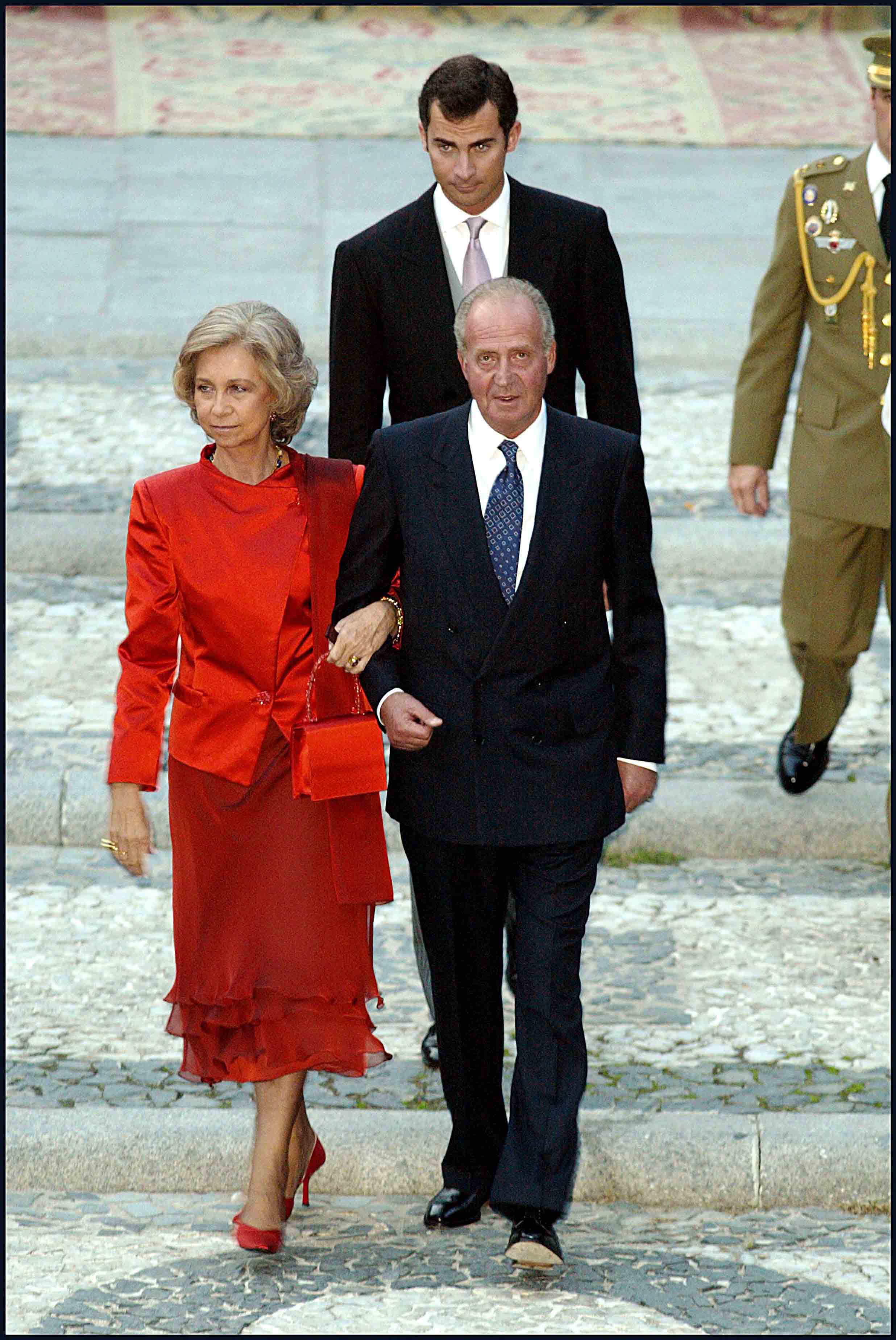 Para una boda, Doña Sofía se enfundó en un conjunto totalmente rojo. La chaqueta, confeccionada en satén, de manga larga y cuello alto. La falda, de gasa y corte midi, decorada con dos volante. Eligió zapatos y bolso del mismo tono. 