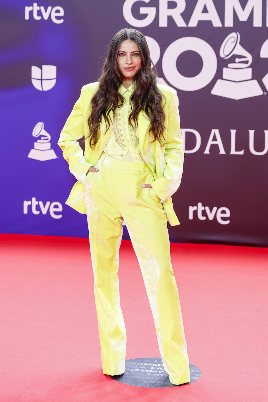La cantante Debi Nova con un traje de chaqueta y pantalón de color amarillo en la alfombra roja de los Grammy Latinos 2023. 