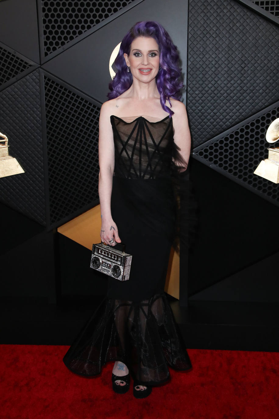 Kelly Osbourne con vestido negro y original bolso en forma de radio-cassette. 