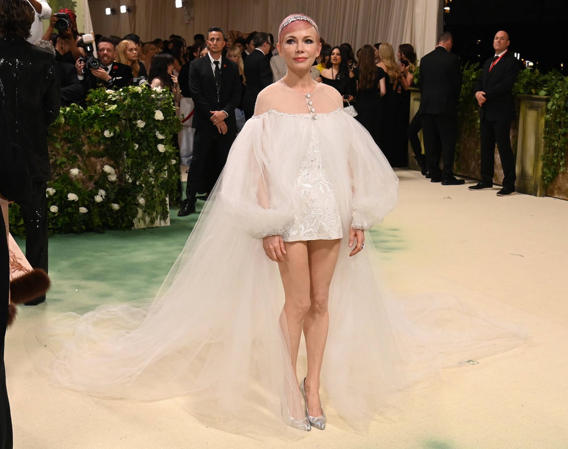 Michelle Williams con mini vestido en color blanco acompañado de una capa de tul XXL de Chanel. La actriz lució su cabello teñido de rosa y adornado con una diadema-joya. 