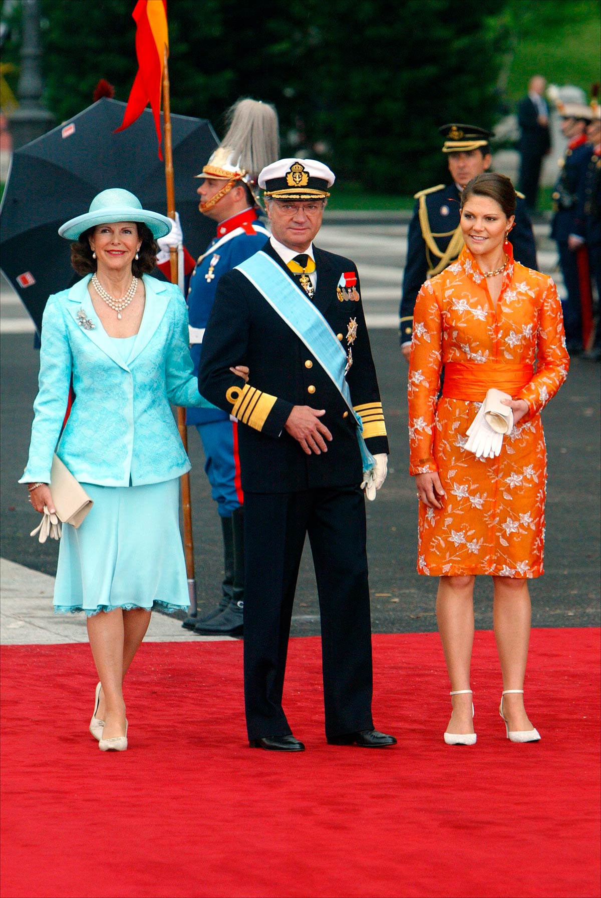 La Princesa Victoria de Suecia se decantó por un vestido naranja con bordados en blanco de inspiración oriental. Su madre, la Reina Silvia llevó un vestido, una chaqueta y una pamela en color azul. 