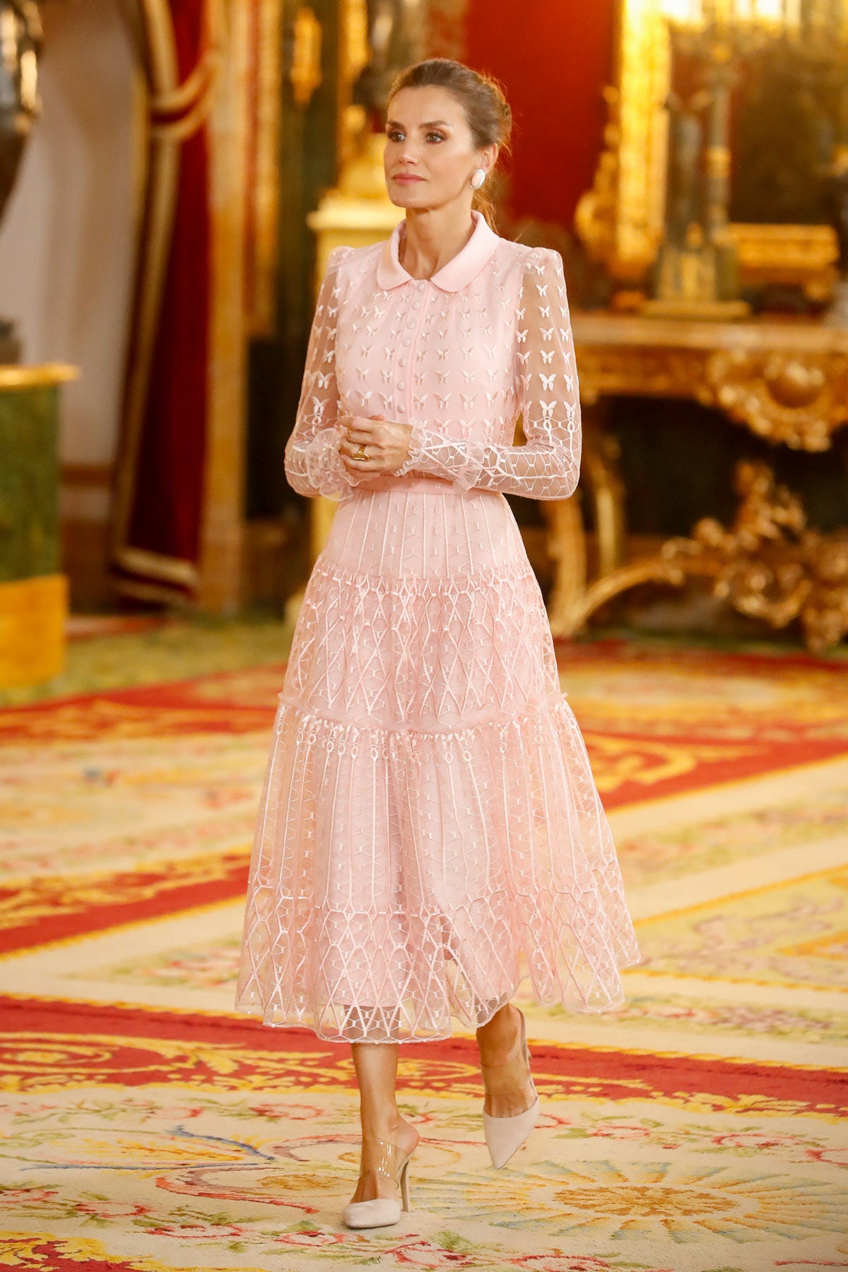 Para el Día de la Hispanidad en el año 2019, la Reina Letizia se enfundó en un maravilloso vestido de Felipe Varela, uno de sus diseñadores favoritos. El atuendo, en color rosa palo, estaba confeccionado en tul y seda y estaba compuesto por un cuerpo camisero con bordados, transparencias en las mangas y una falda con vuelo. Lo remato con unos mules semitransparentes de Steve Madden y un clutch fucsia de Magrit. En el pelo, lució un moño. 