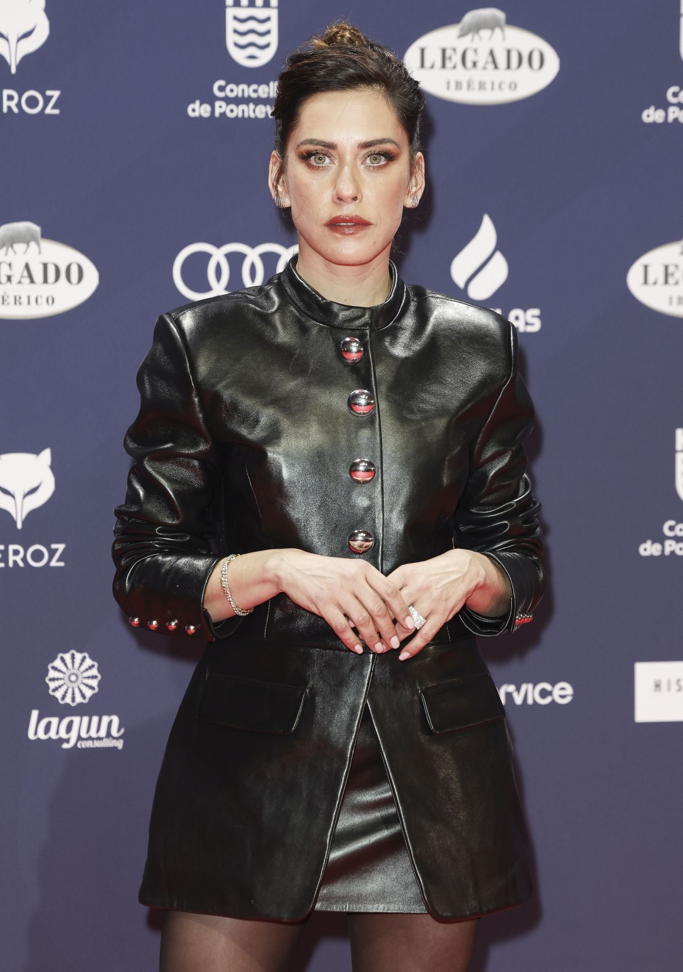 La actriz María León ha apostado por una una chaqueta larga en cuero con bolsillos y botones joya combinada con una minifalda en el mismo tejido. 