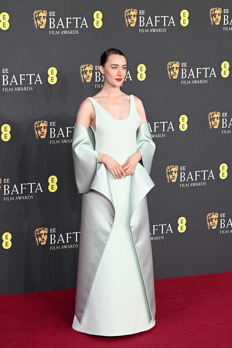 Saoirse Ronan llevó un vestido de crepé de color verde pálido con una estola de satén doble de seda y sandalias de satén a juego de Louis Vuitton. completó su estilismo con un recogido y labios rojos.