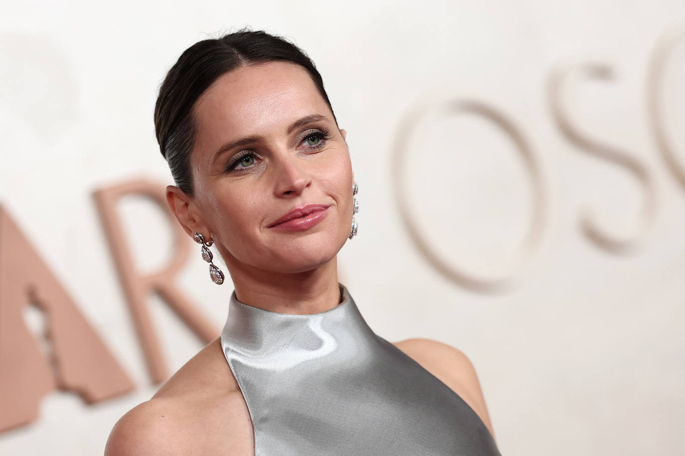 Felicity Jones con moño de bailarina, sombras grisáceas y labios naturales. 