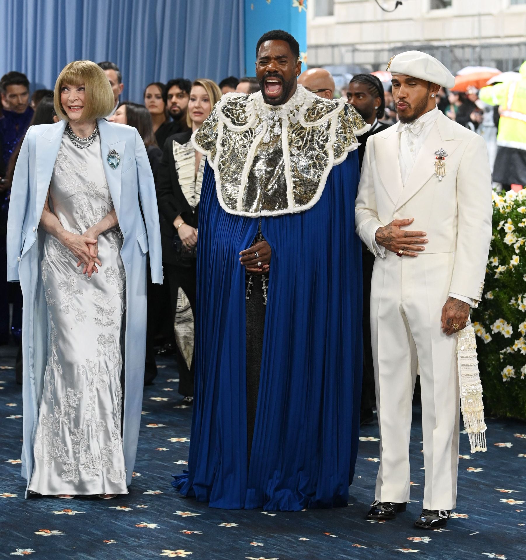 Anna Wintour con abrigo azul y vestido plata de Louis Vuitton. Junto a Colman Domingo y Lewis Hamilton quien ha llevado un esmoquin blanco con boina de Grace Wales Bonner.