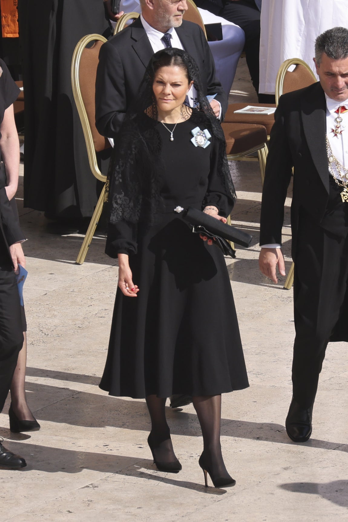 La princesa Victoria de Suecia también cumplió con el protocolo, eligiendo un look de luto. Lució un vestido midi de manga larga, mantilla, medias y salones negros. Como joyas, eligió un discreto colgante y pendientes de perlas. Además, lució en la solapa una de sus condecoraciones, como heredera al trono.