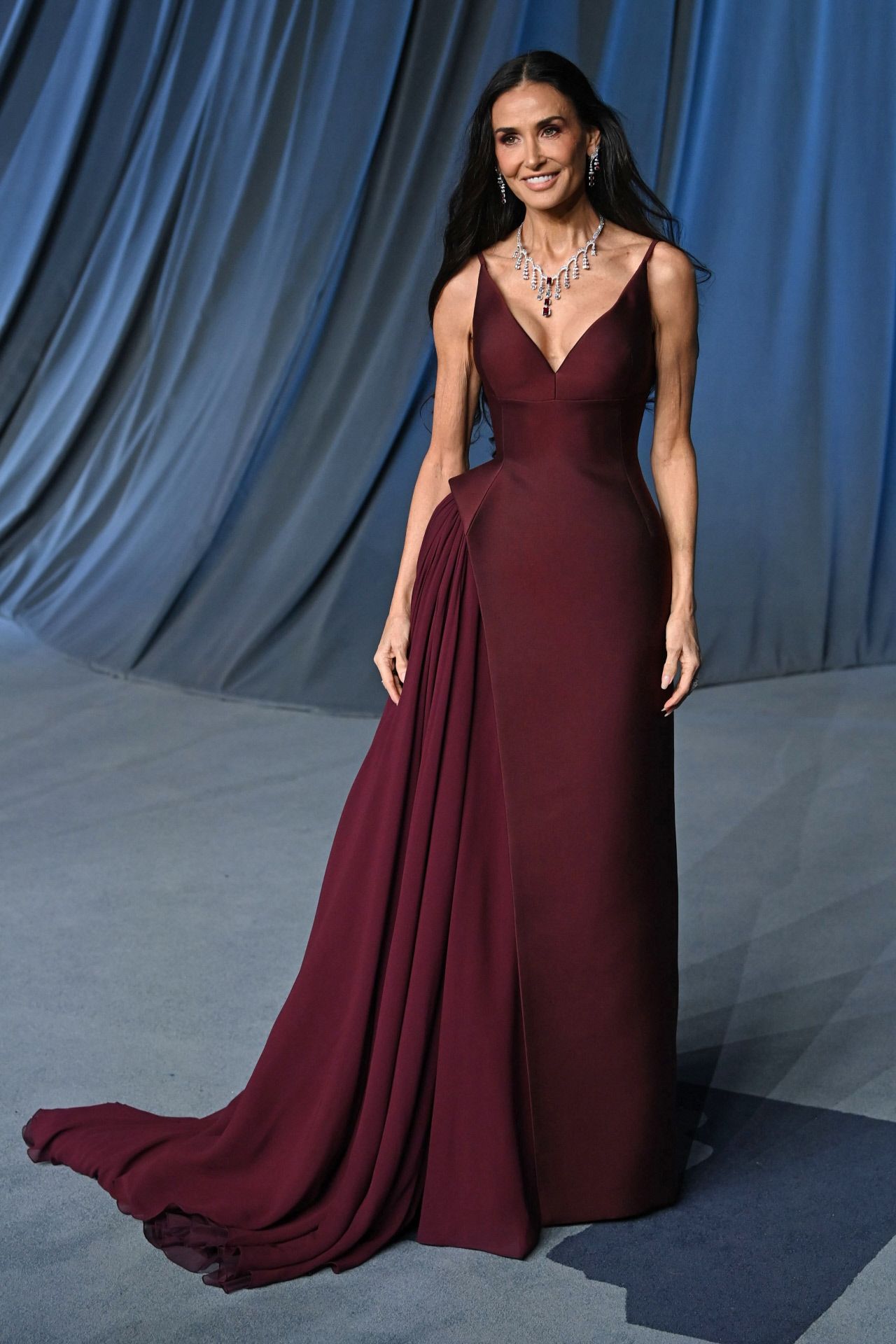 Demi Moore apostó por un vestido burdeos con volumen lateral y cola de Prada, que combinó con un gran collar y pendientes a juego. 