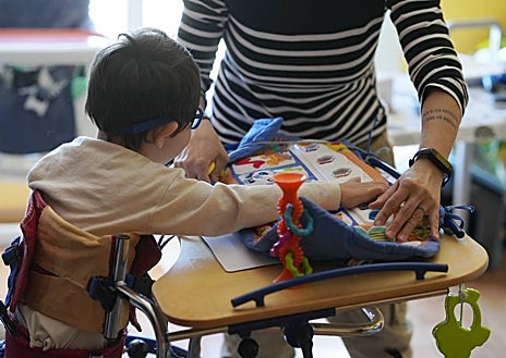 Imagen secundaria 1 - Eduardo en su bipedestador junto a su hermana Paula (arriba). El pequeño juega en su mesa especial (abajo a la izquierda). María sostiene a su hijo en pie mientras Estefanía juega con él (abajo a la izquierda)