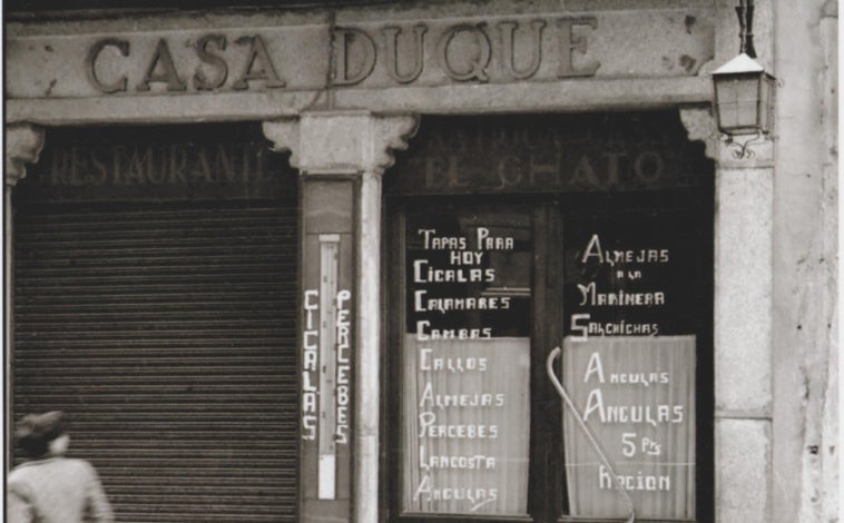 Imagen principal - Sobre estas líneas, arriba, foto antiguia de la fachada del restaurante Casa Duque de Segovia, donde se podía leer 'Antigua Casa El Chato', apodo de Dionisio Duque, primera generación de la familia y fundador de Casa Duque. Abajo, a la izquierda, uno de los salones del restaurante en 1928. A la derecha, Julián Duque, segunda generación de la saga familiar en la puerta de la calle Cervantes 12 de Segovia en la que siempre ha estado ubicado este negocio.