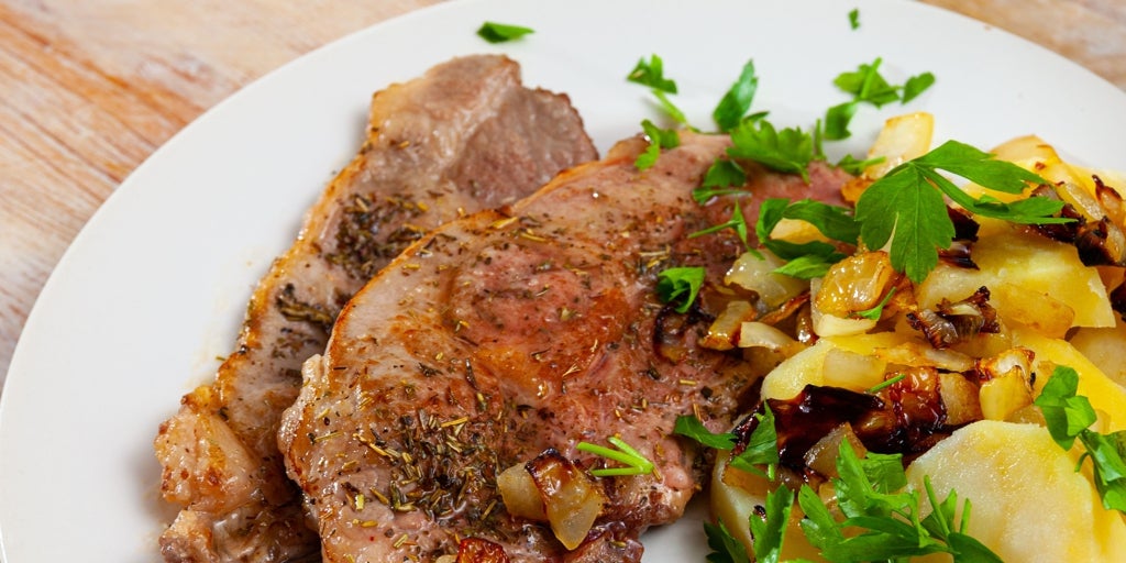 Chuletas de pavo acompañadas de patatas con tomate, orégano, cebolla y salsa tzatziki