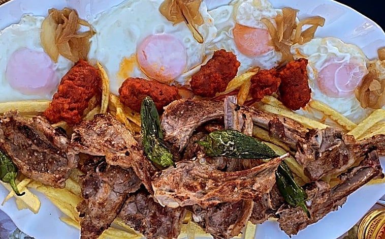 Imagen principal - Imágenes de la Bodeguita Nicomedes: Plato de huevos fritos con patatas, chuletitas de cordero, chorizo y pimientos, bocoyes donde fermentan el vino joven y tabla de chacinas con mosto