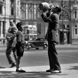 Un adolescente bebe de un botijo frente al Palacio de Comunicaciones de Madrid, en 1952