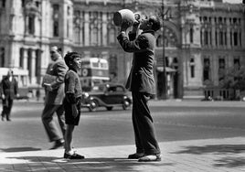 Un adolescente bebe de un botijo frente al Palacio de Comunicaciones de Madrid, en 1952