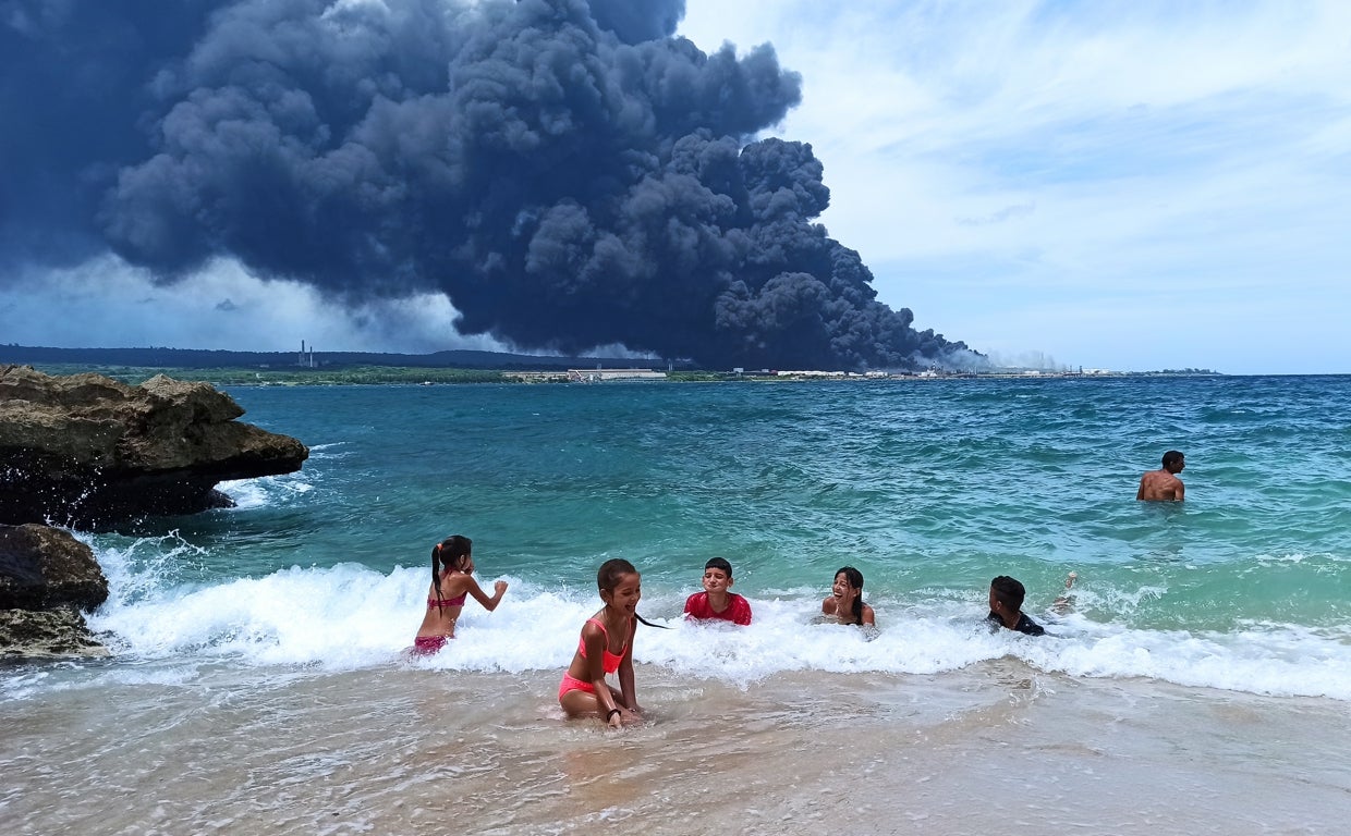 Bañistas en el mar mientras al fondo se ve la columna de humo provocada por el incendio en Matanzas