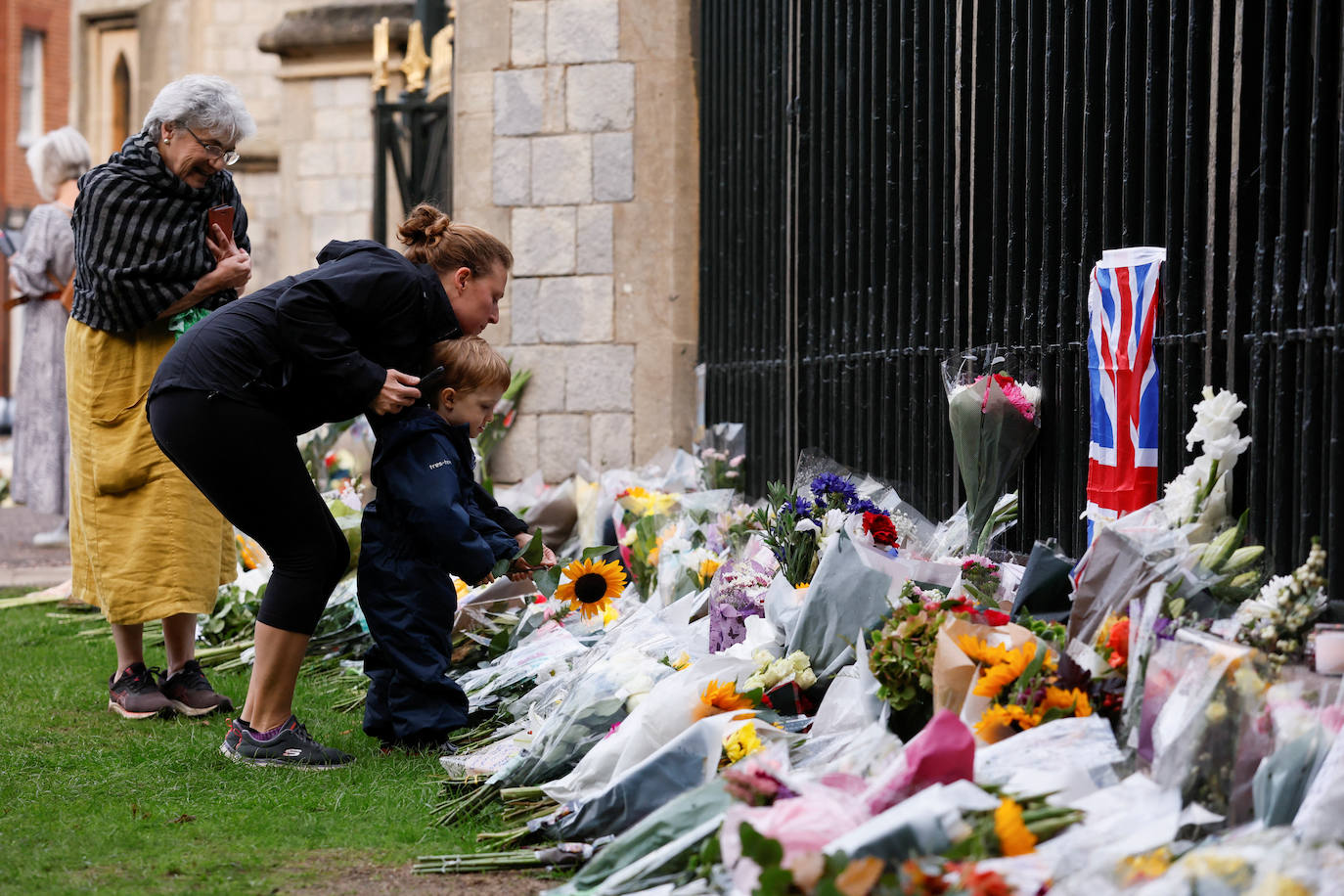 Un niño deposita un ramo de flores junto a su madre